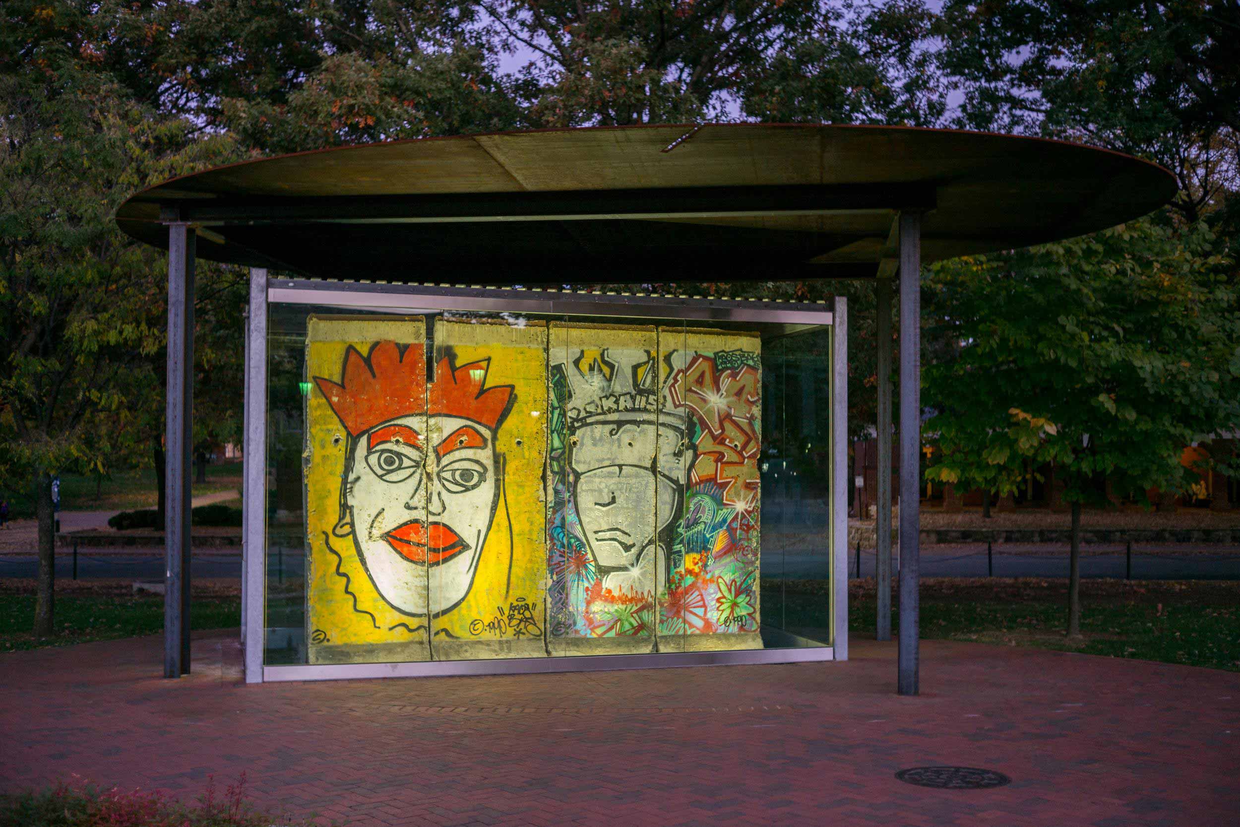 Four panels of the Berlin Wall — featuring two depictions of kings, one colorful and another rendered in gray — stand on Grounds near the Albert and Shirley Small Special Collections Library.