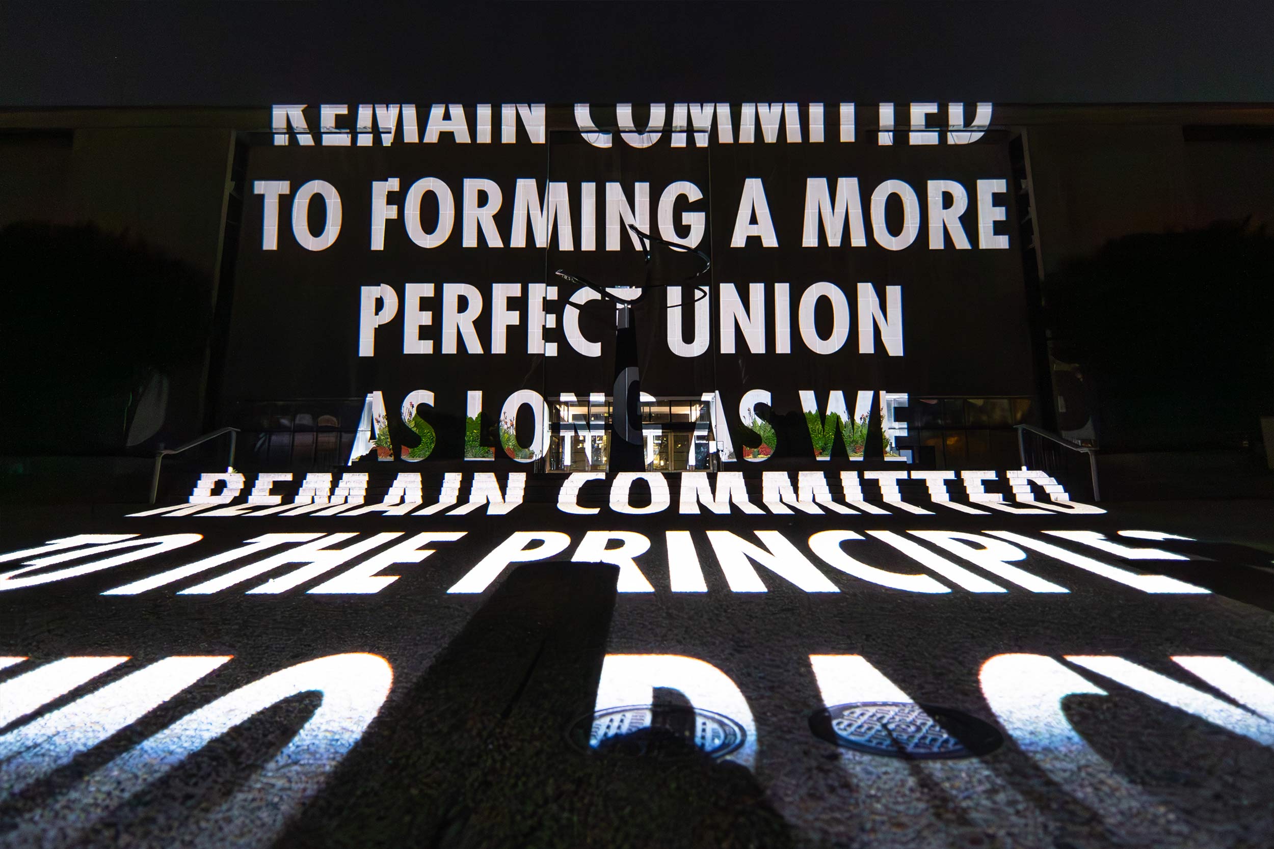 The following words are projected onto the ground and on a wall surrounding stairs and two sets of doors at the National Mall: "Remain Committed to forming a more perfect union as long as we remain committed to the principles [of] democracy..."
