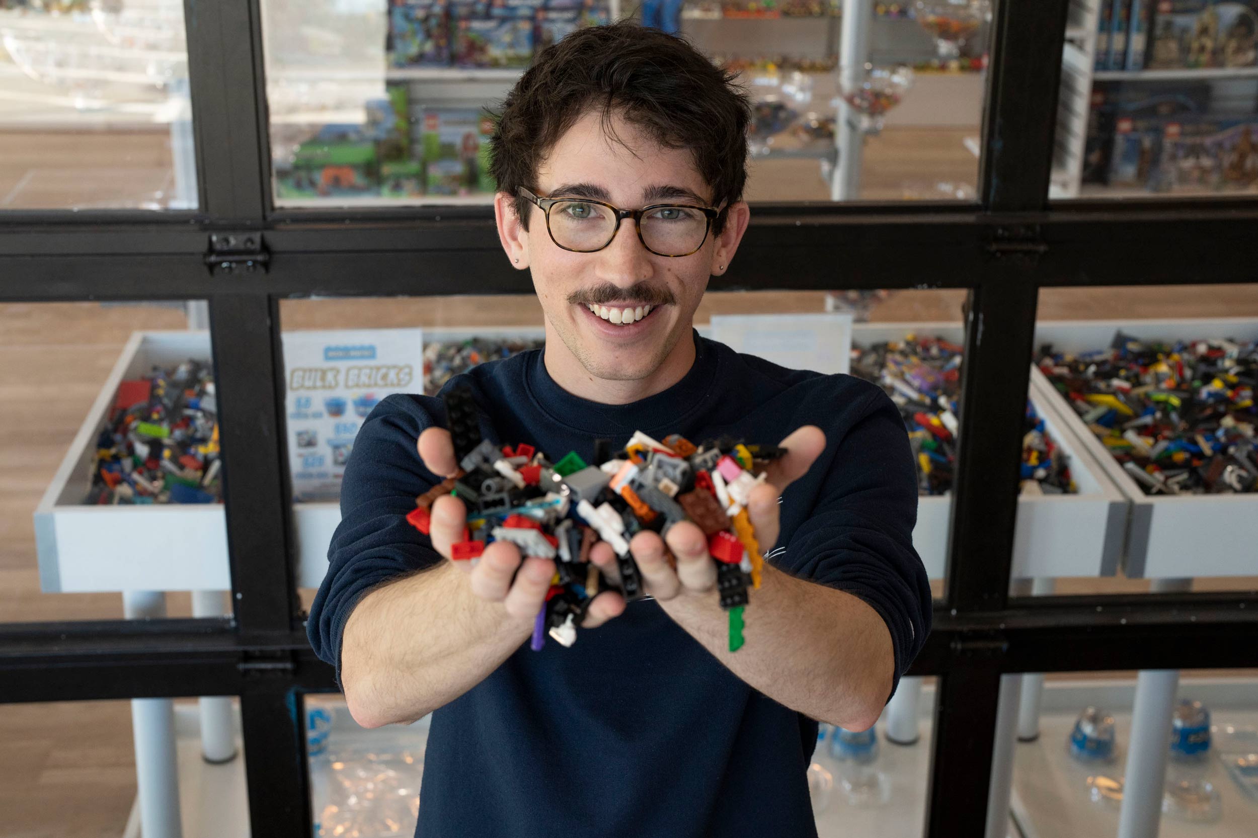 Ben Edlavitch smiles at the camera and holds up two handfuls of legos.