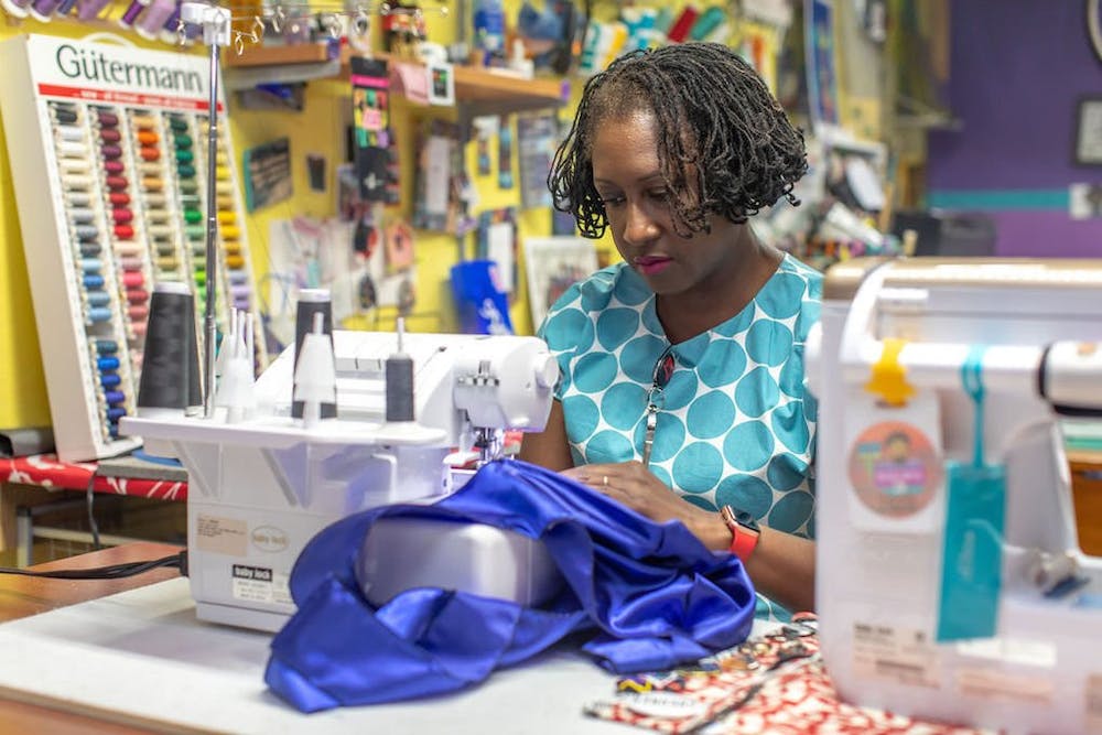 Professor Lisa Woolfork uses a sewing machine to stitch a shiny blue-purple fabric.