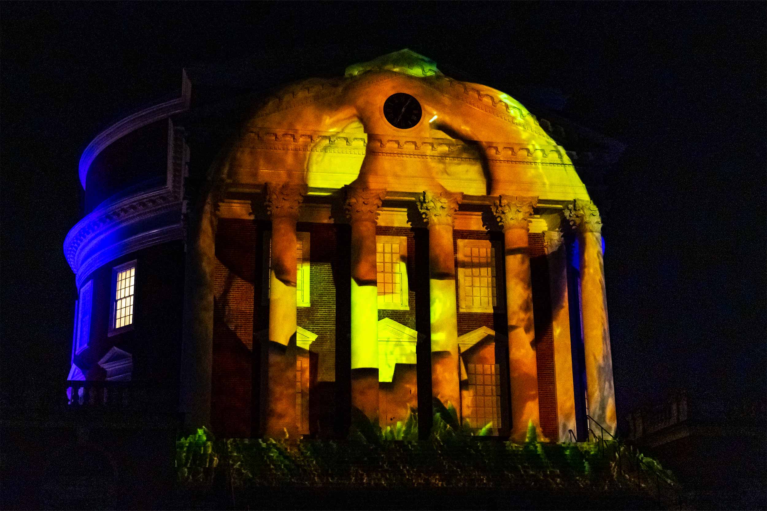 A projection of a smiling orange Jack-O-Lantern on the Rotunda at night.