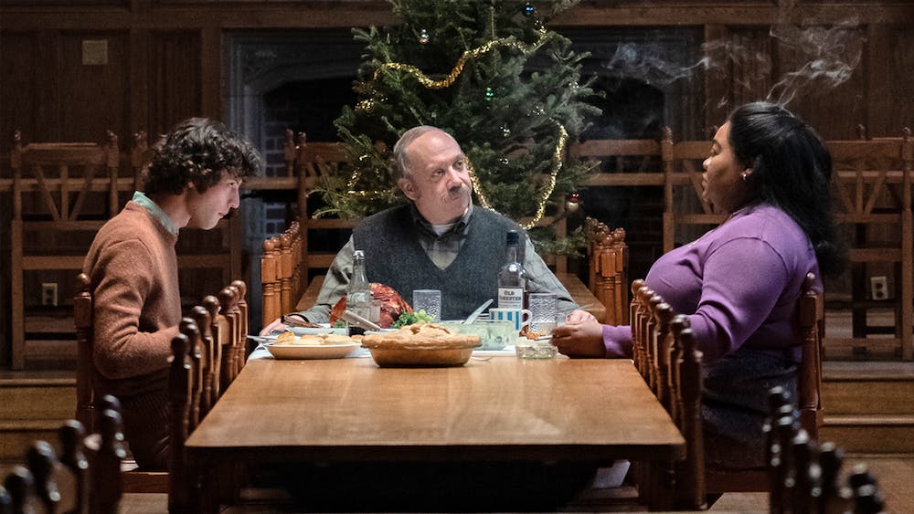 A still from "The Holdovers" shows Paul Giamatti, Dominic Sessa, and Da'Vine Joy Randolph sit at a table eating dinner.