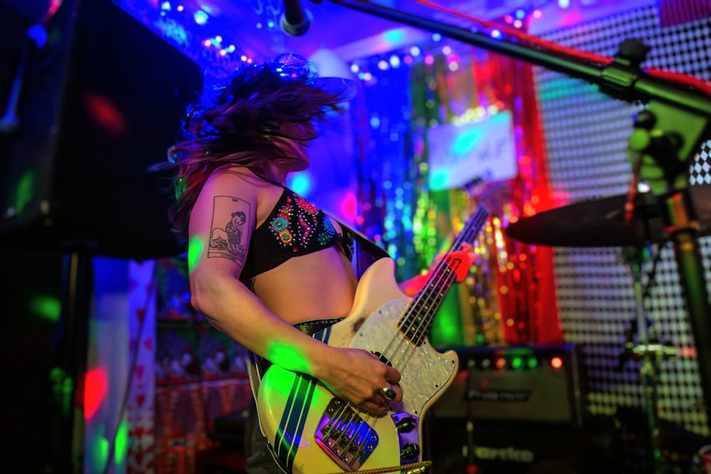 A musician plays a guitar, surrounded by sound equipment and multicolored lights 