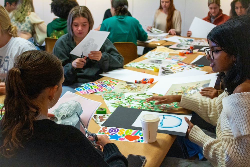 Artists create posters at a table filled with paper, stickers, and drawings.