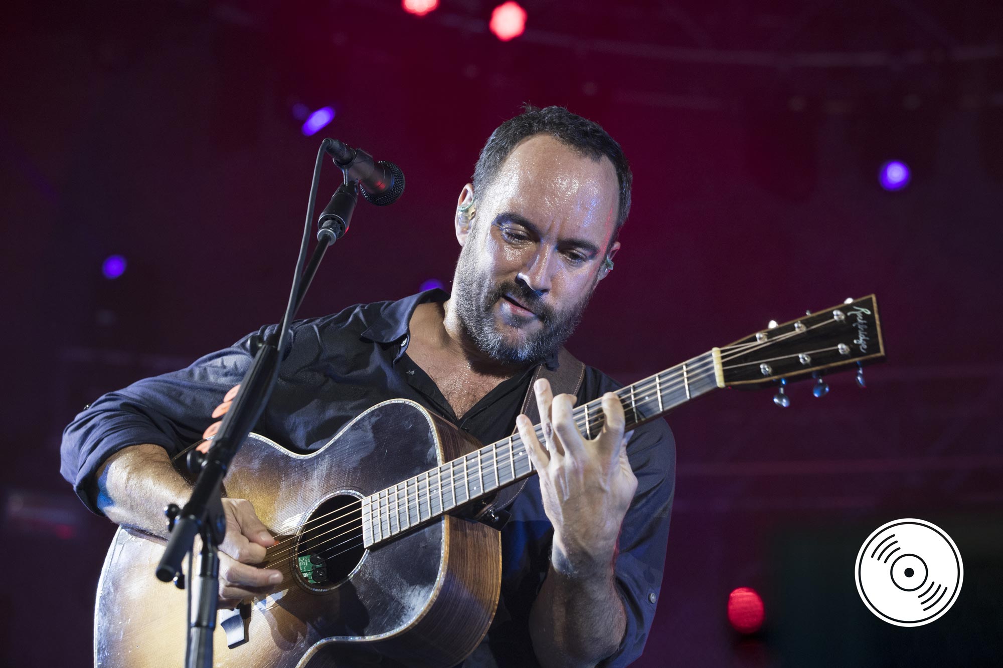 Singer Dave Matthews plays an acoustic guitar onstage in front of a microphone.