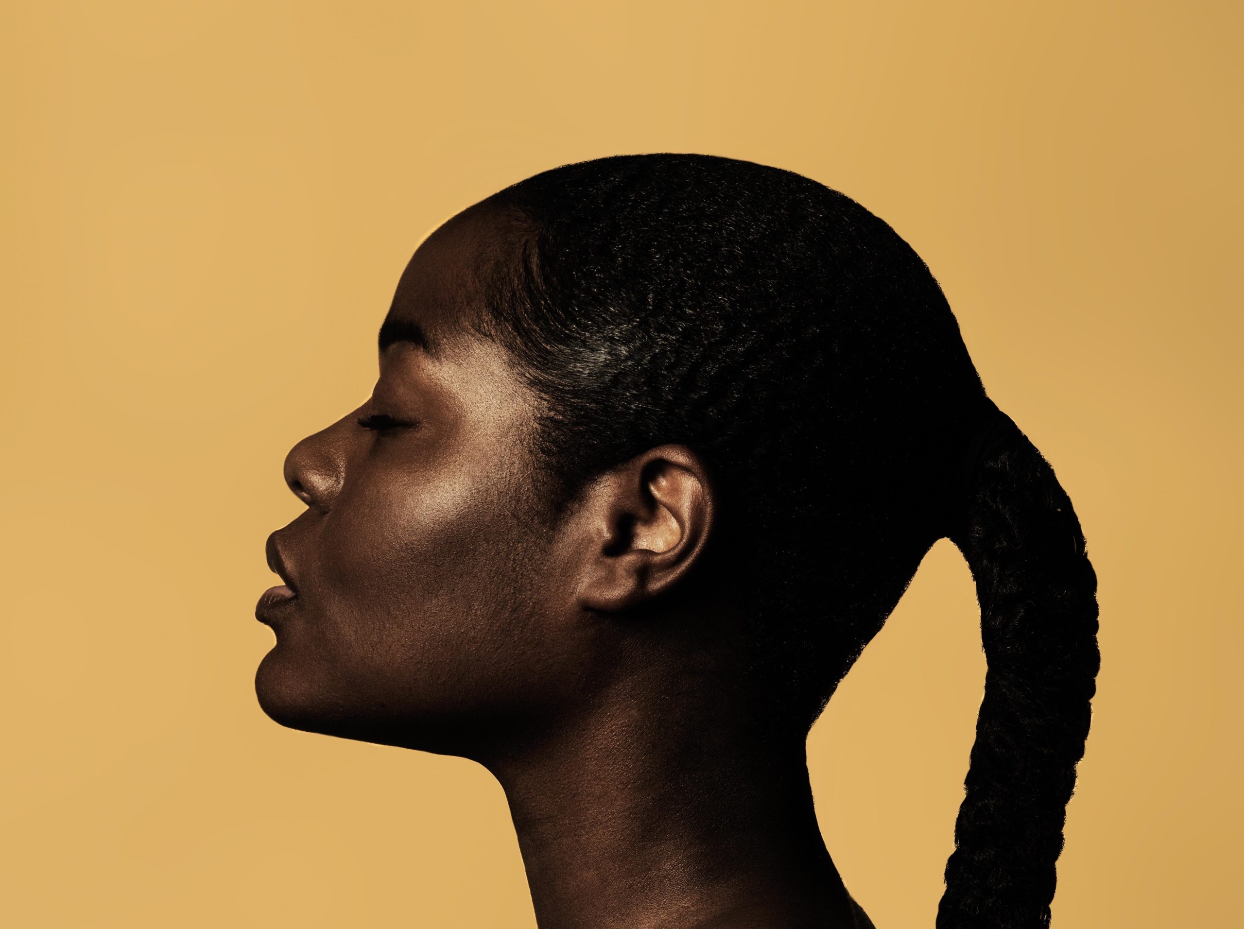 The profile of a black woman with a single braid against a yellow background.