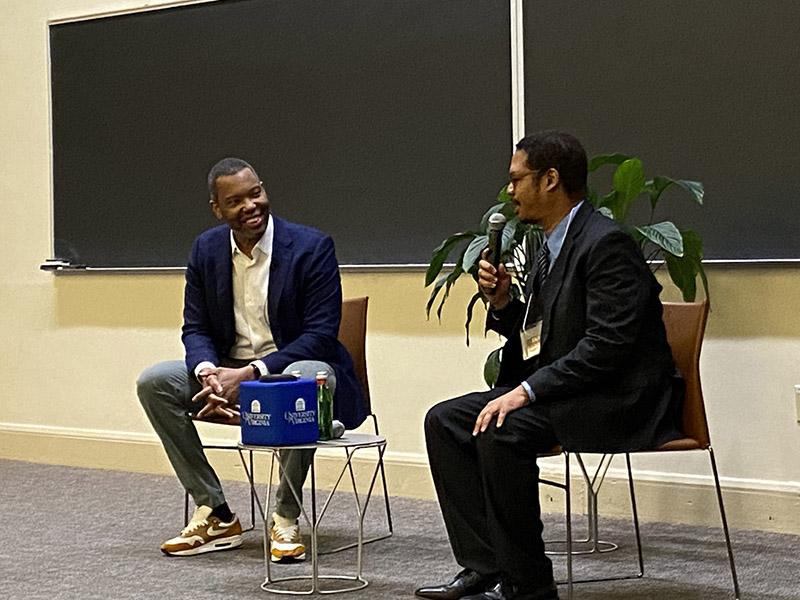 Ta-Nehisi Coates sits in a chair and speaks to Robert Greene, who sits and speaks into a microphone.