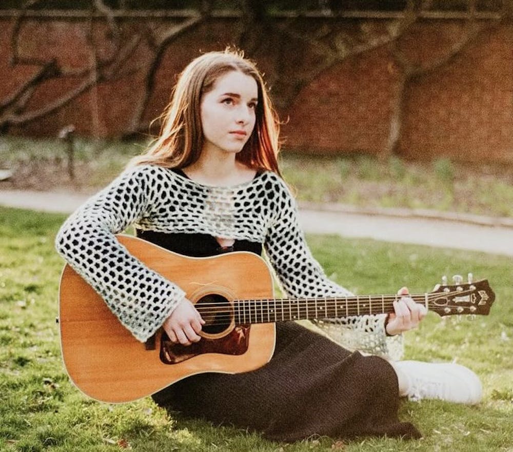 First-year Niamh Kierans sits on the ground in a garden and strums a guitar.
