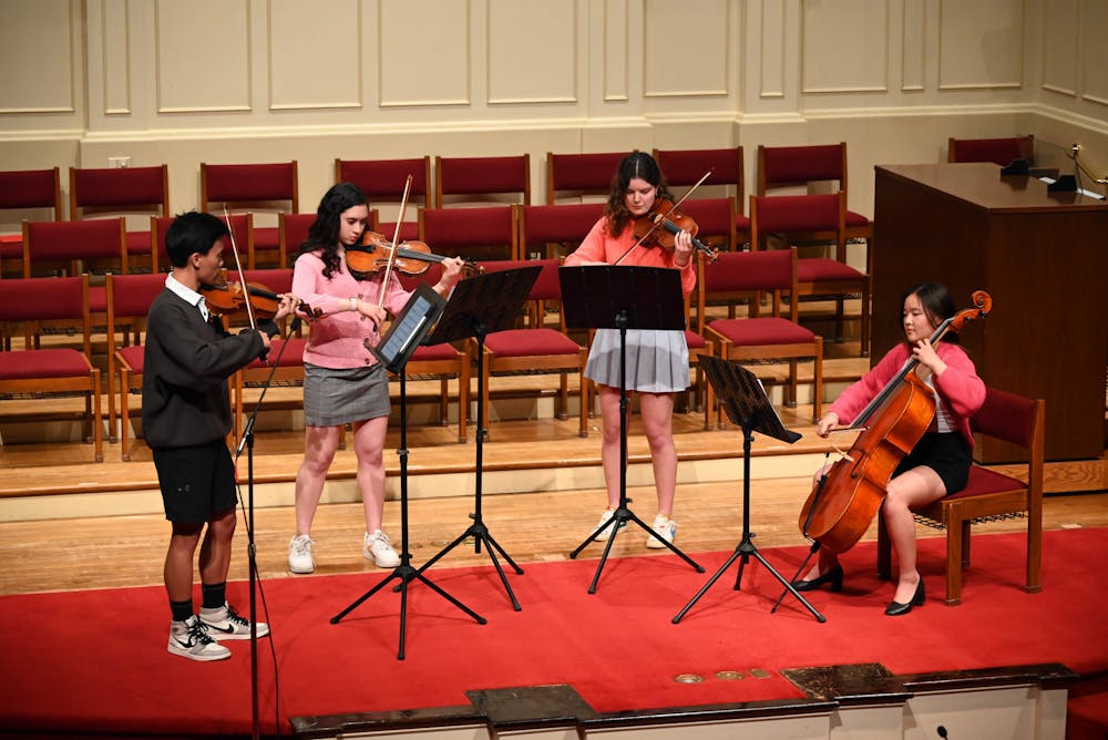 Four students in the Radio Music Society stand in a circle and play string instruments, reading sheet music on a stand.