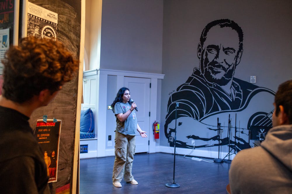 UVA student Tara Sury holds a microphone and stands on the stage of 1515, next to a large mural of Dave Matthews on the wall.