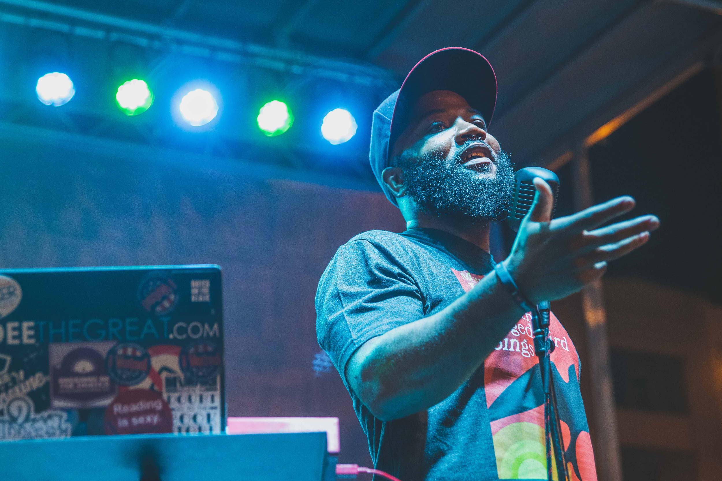 Professor A.D. Carson wears a baseball cap and stands in front of a microphone, backed by stage lights.