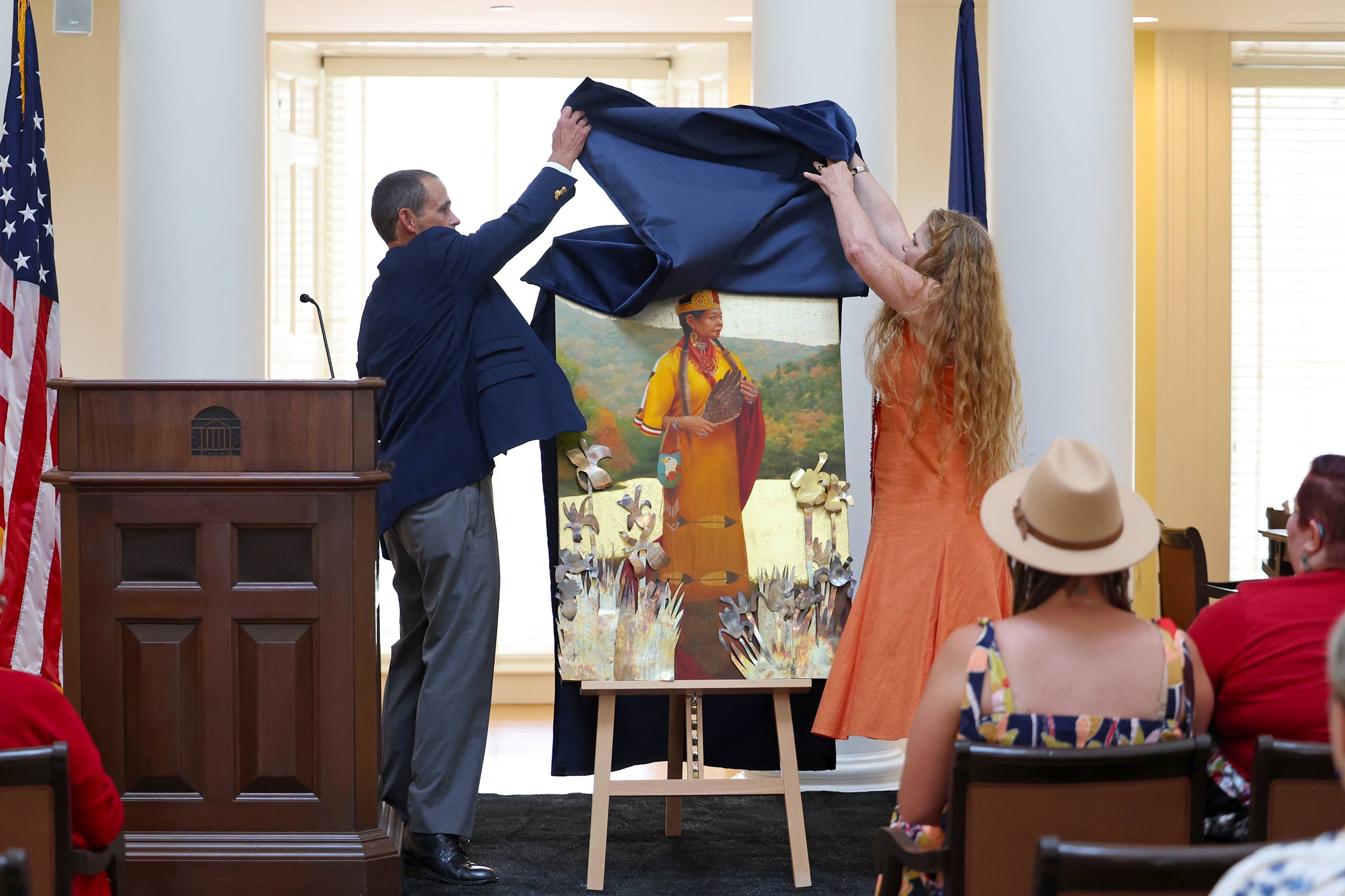 In the dome room of the Rotunda, Jim Ryan and Teresa Pollack pull a blue covering off of a painting of Karenne Wood. In the portrait, she wears a yellow dress and Monacan regalia, and holds  