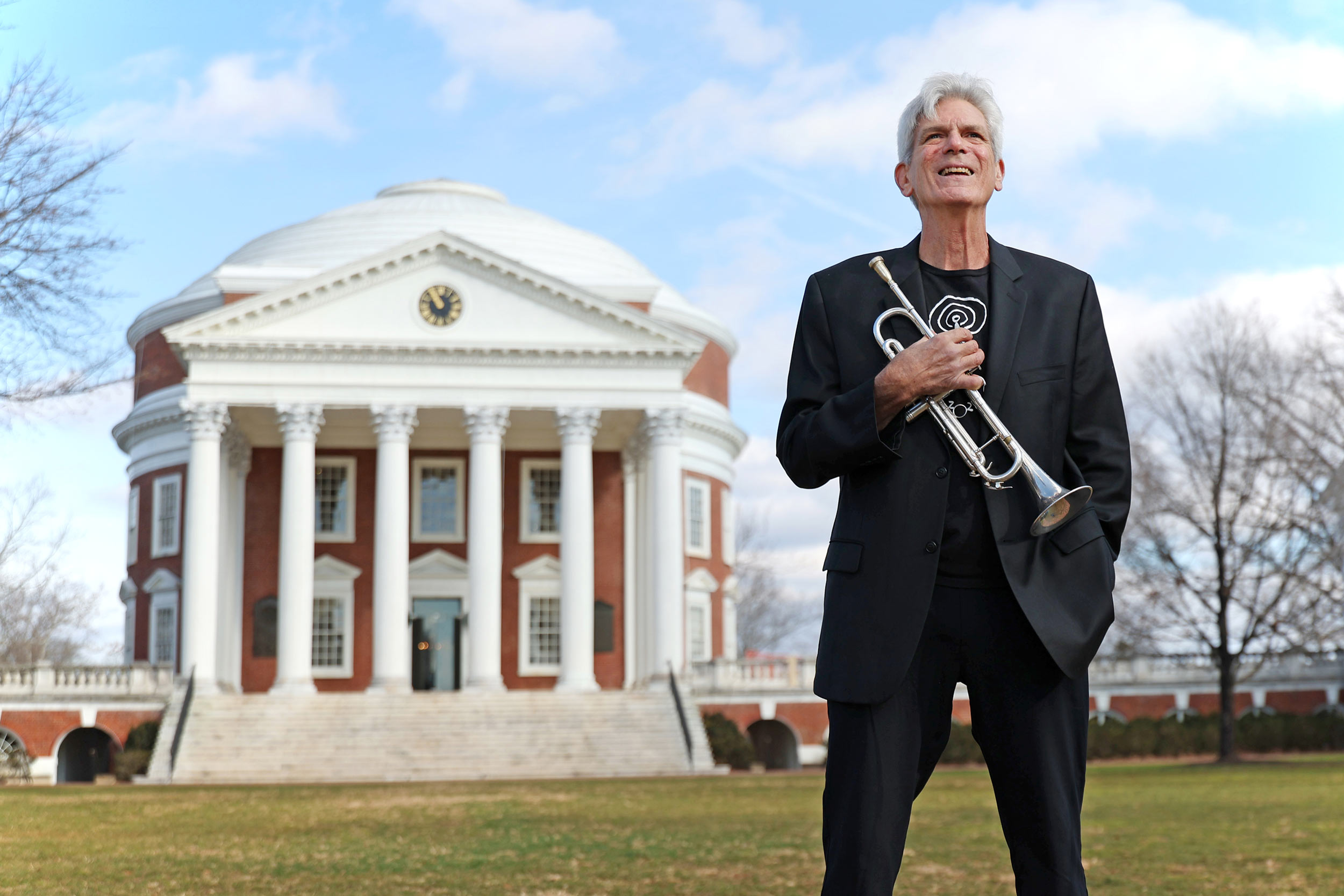 John D'Earth, holding a trumpet to his chest, looks up at the sky while standing in front of the Rotunda.