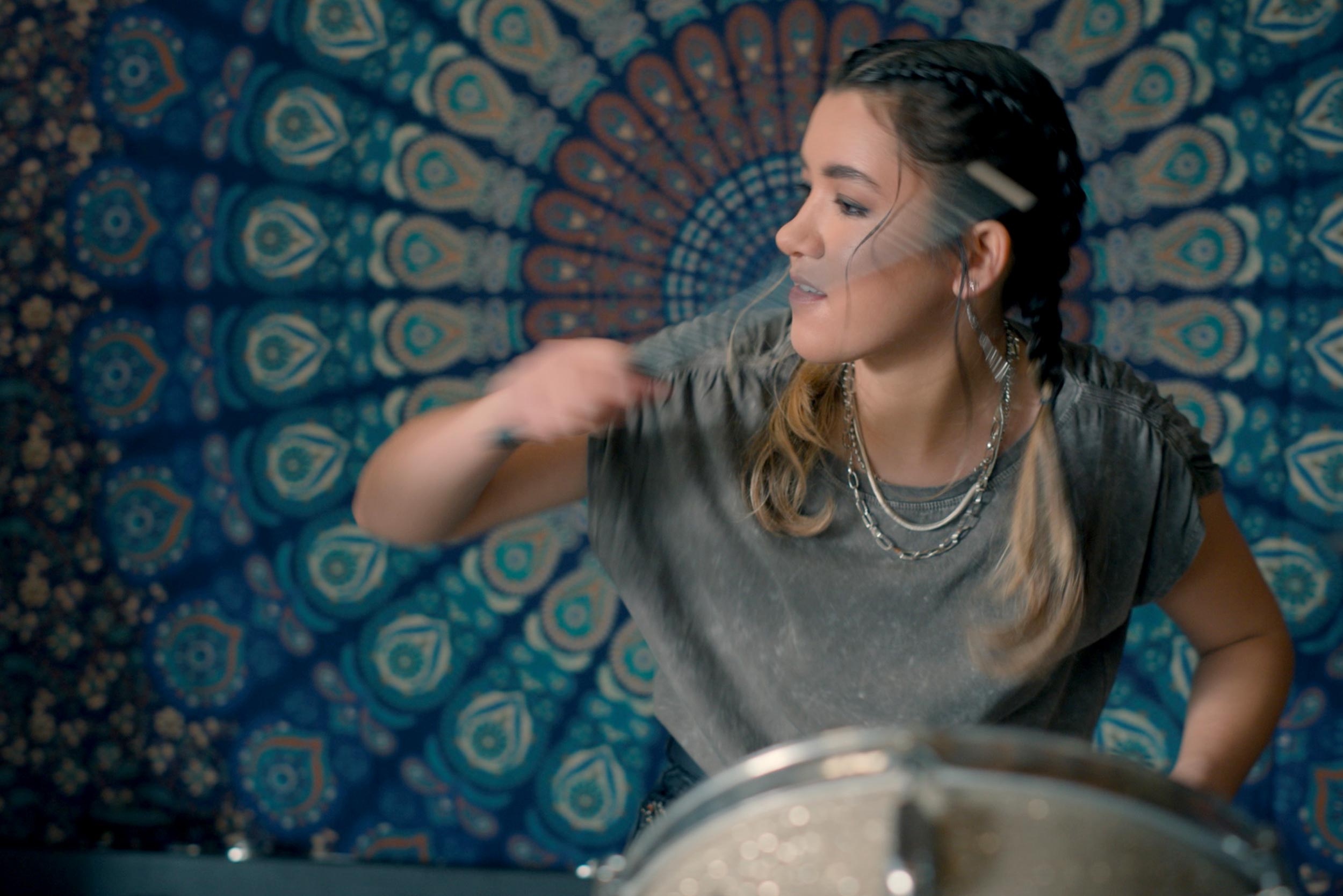 Elena Heraldo plays the drums in front of an ornately patterned background.