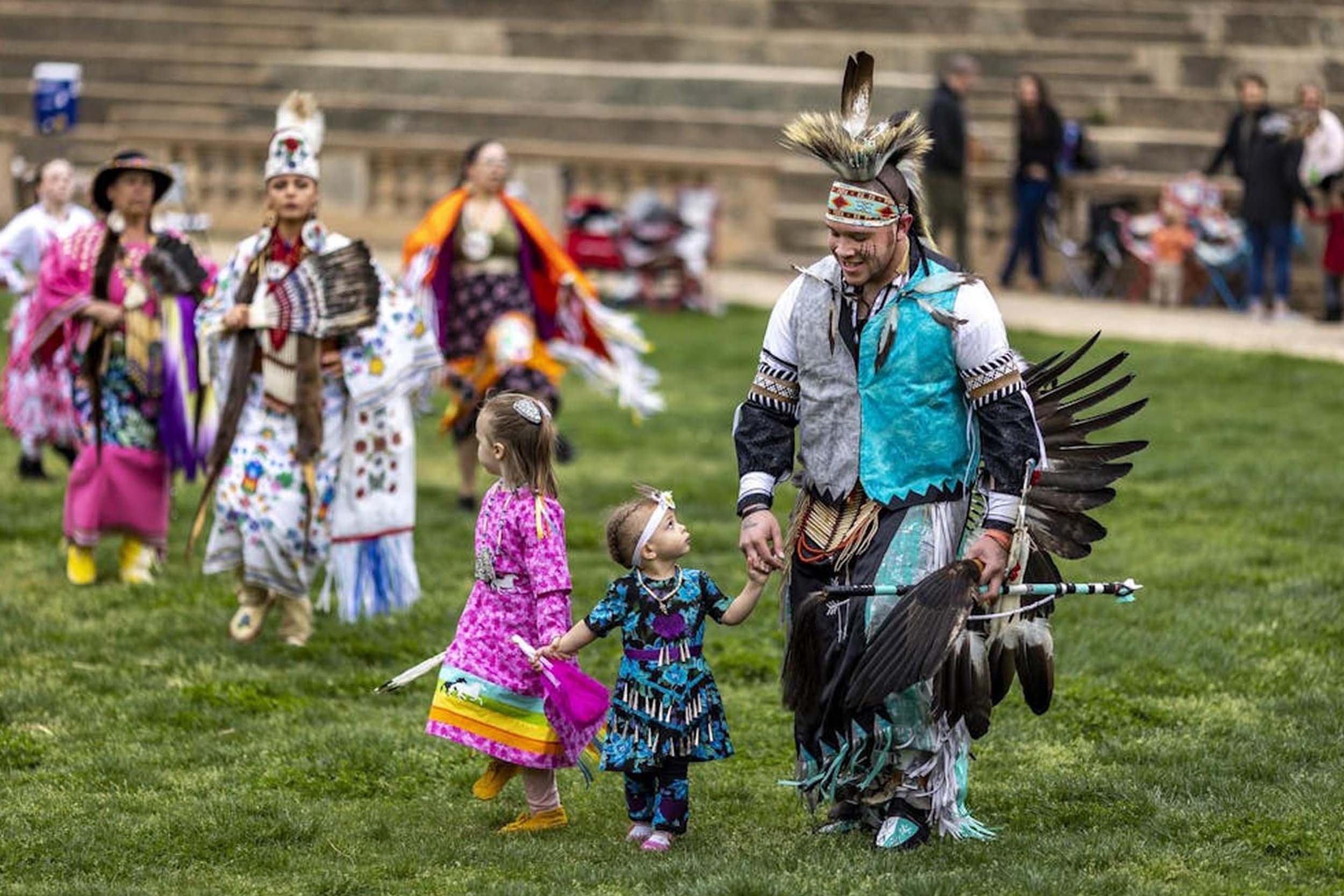 Adults and children in traditional clothing walking across the amphitheater.