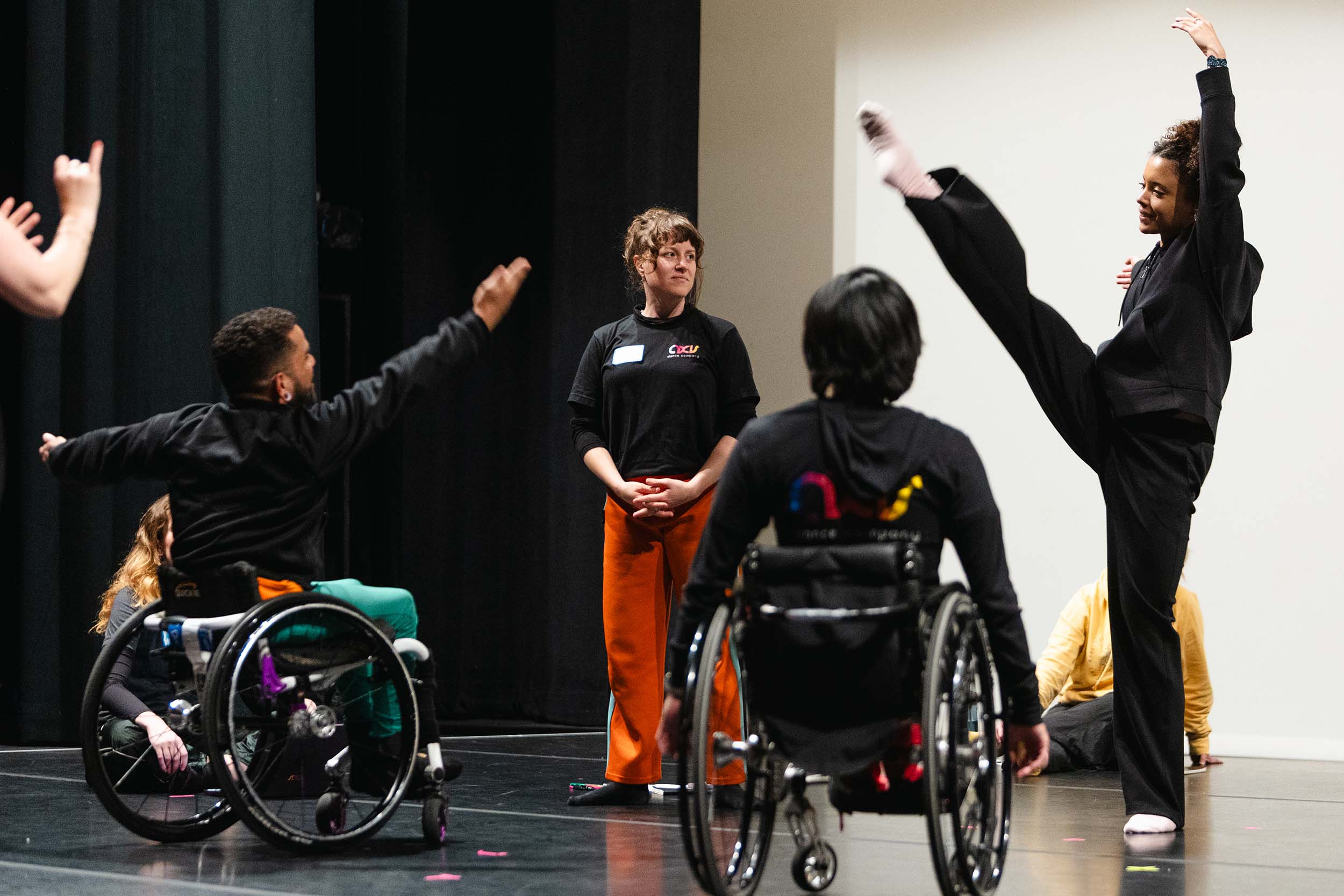 Group of dancers rehearsing, one kicking and two in wheelchairs.