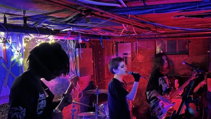 A basement show with band members performing, red and blue hues of light fill the space.